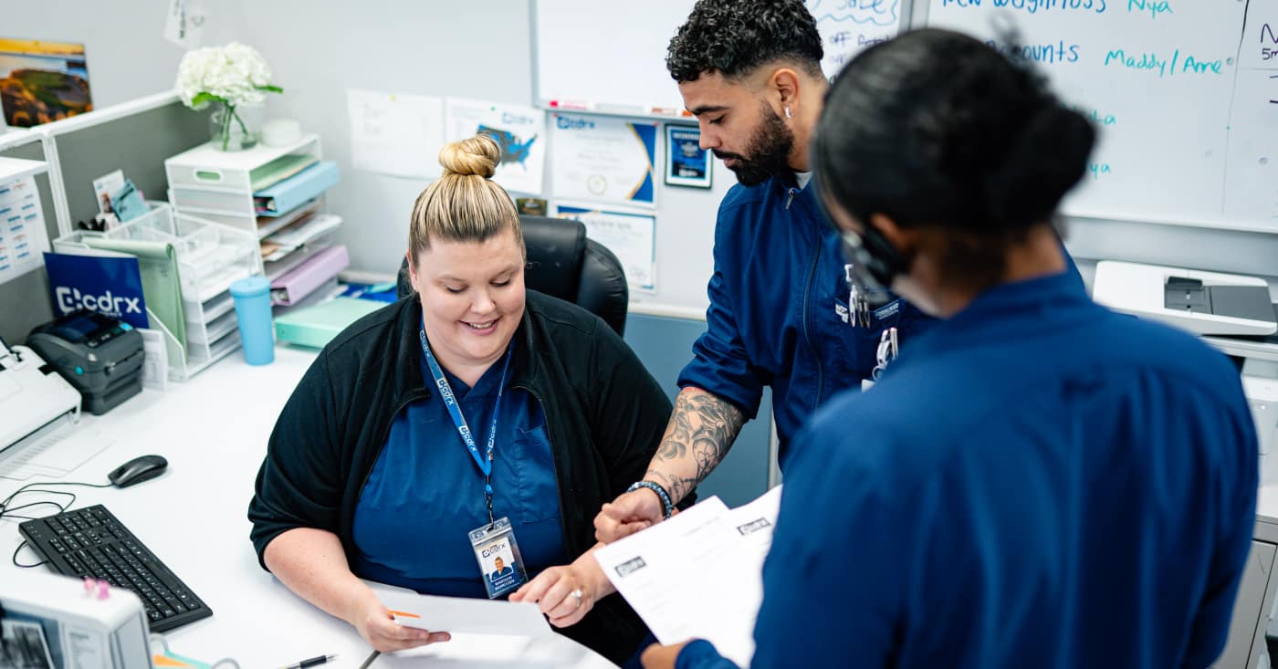 Smiling Cdrx Worker Reviewing Documents With Colleagues At Office Desk