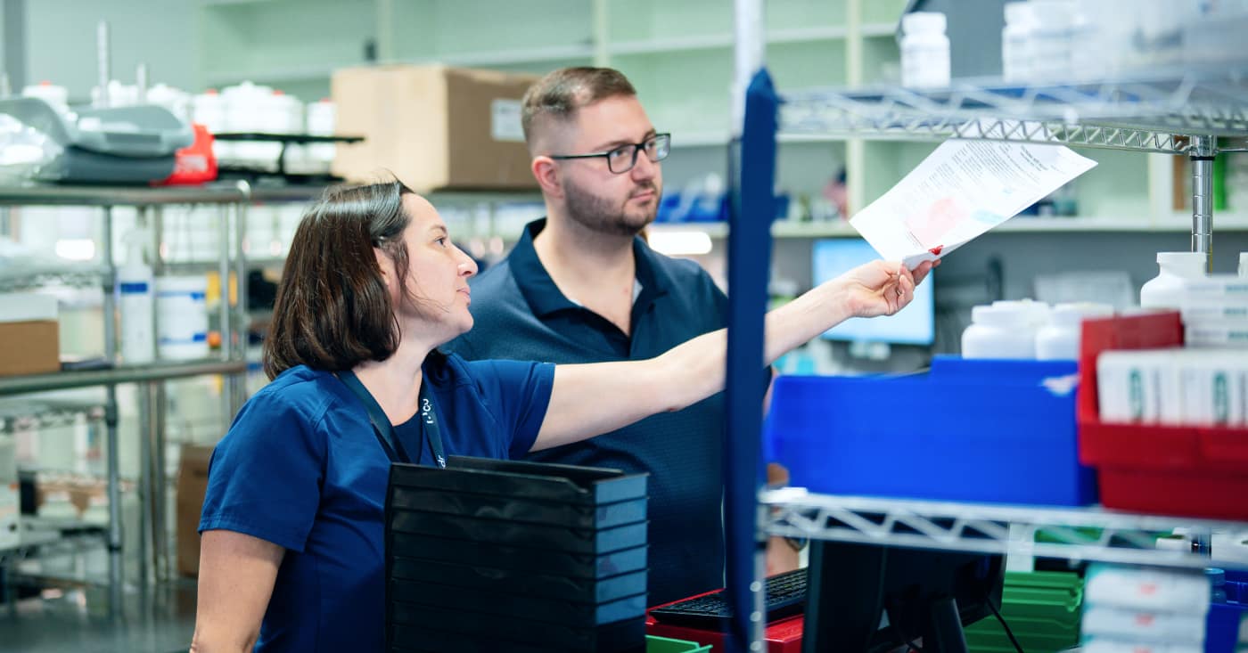 Two Lab Technicians Reviewing Paperwork In Laboratory With Shelving