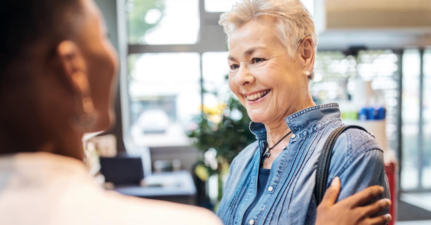 Woman In Denim Shirt Smiling While Talking To Person In Bright Office