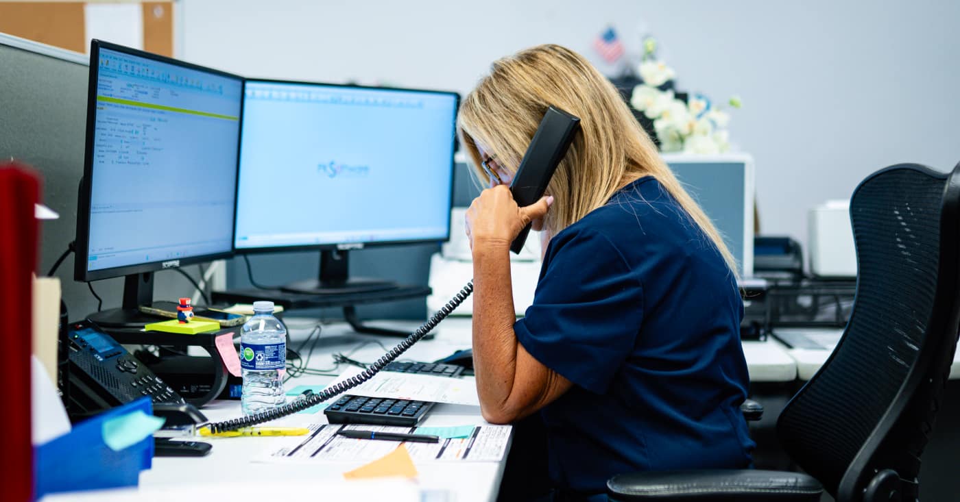 Woman Talking On Phone At Office Desk With Dual Monitors